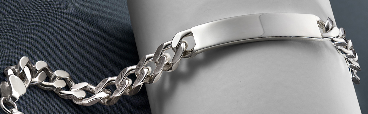 A standout sterling silver gents identity bracelet lying on a white bracelet roll on a dark grey satin background
